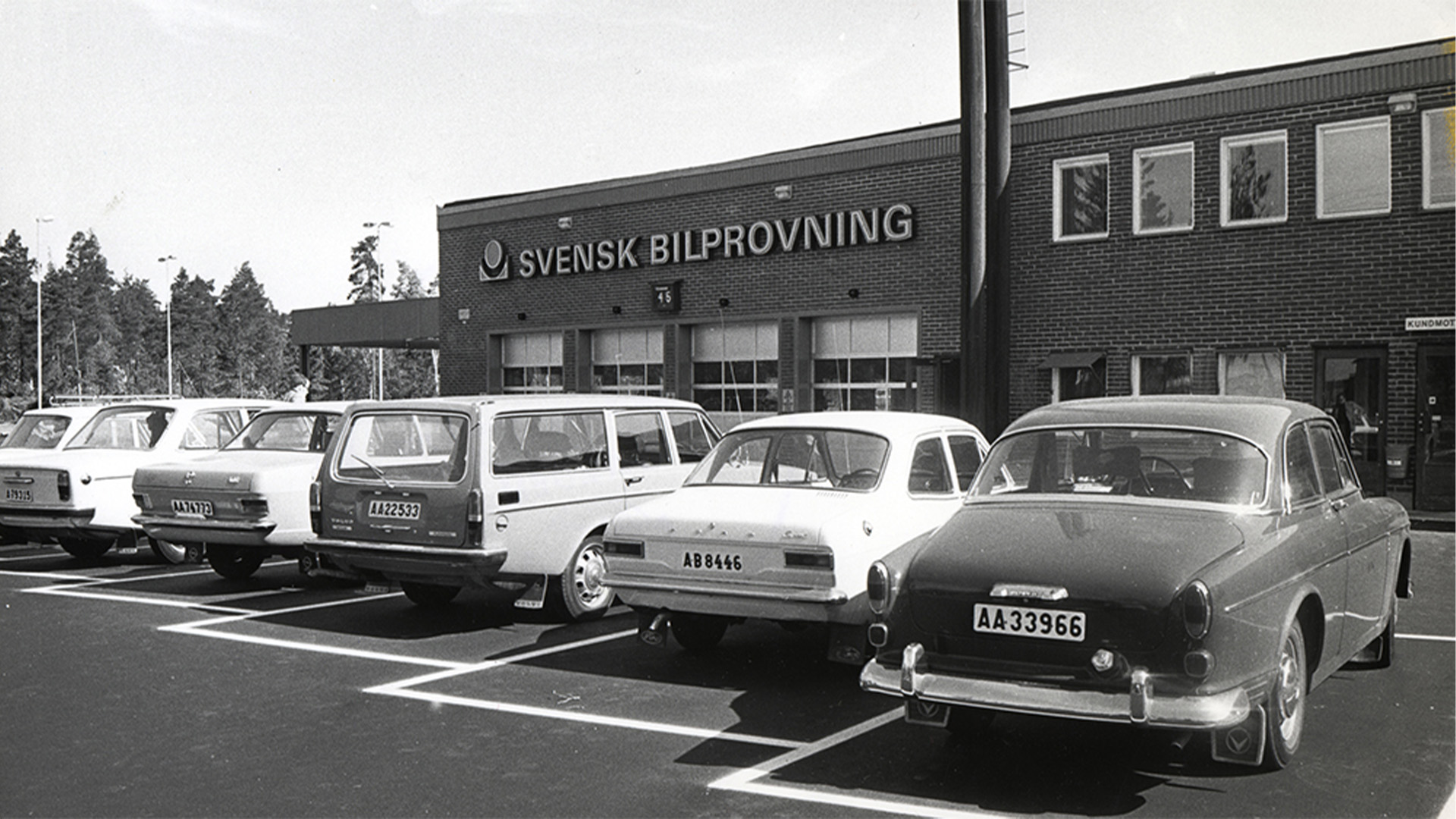 Svartvit bild på bilar som står parkerade framför Bilprovningen.