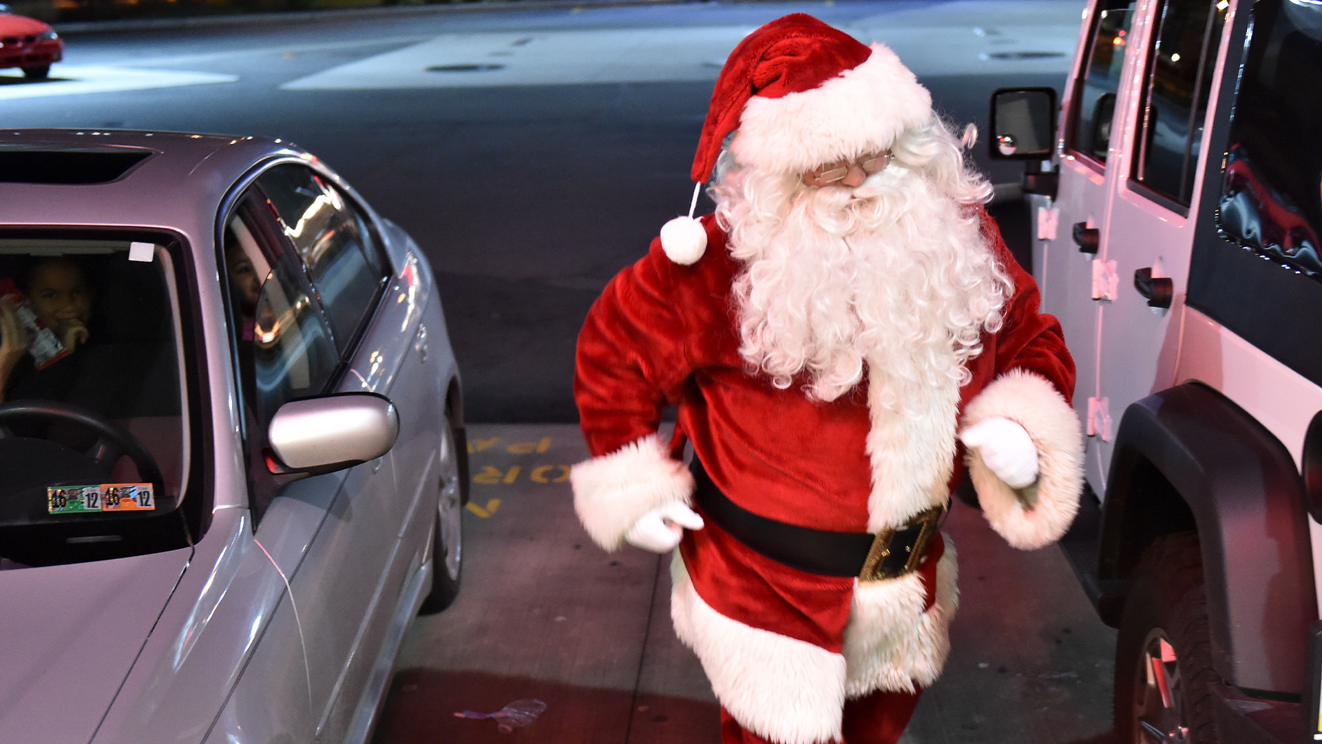 Jultomten går mellan två parkerade bilar.