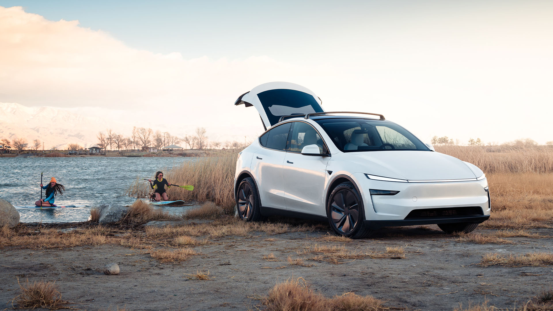Nya Tesla Model Y i vitt står med bagageluckan öppen och två människor paddlar i vattnet bakom.
