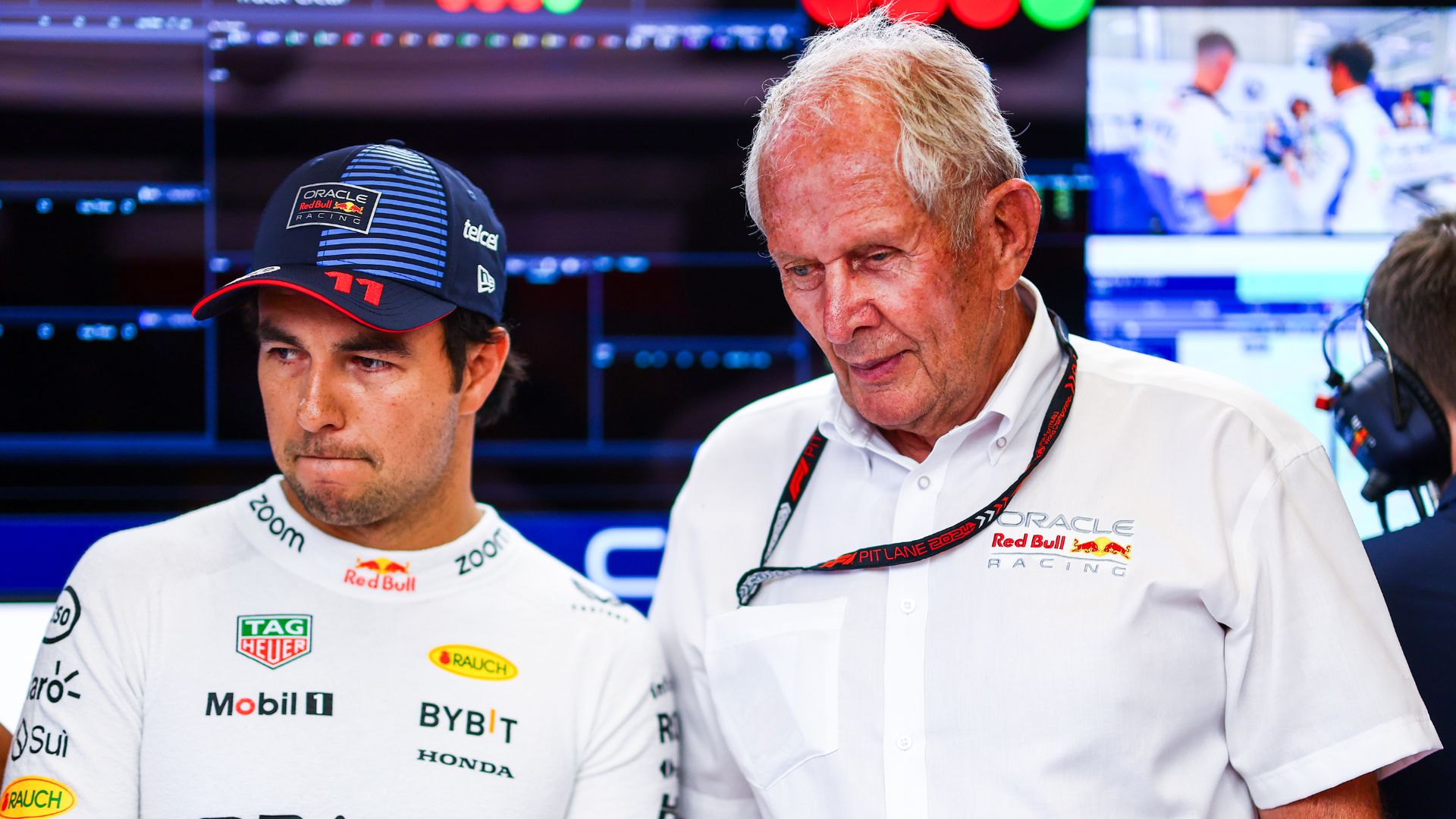 Sergio Perez och Helmut Marko i Red Bulls garage under en Formel 1-helg, med allvarliga uttryck och teknisk utrustning i bakgrunden.