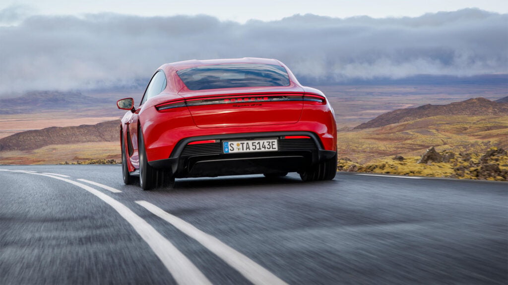 Röd Porsche Taycan kör bort från kameran. Låga moln syns i horisonten.