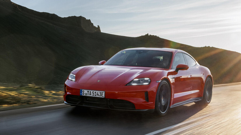 Röd Porsche Taycan kör på väg. Bilden är tagen snett framifrån.